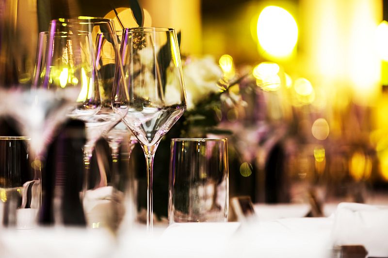 Im Bild zu sehen sind Weingläser, die darauf warten aus den dahinter stehenden Flaschen egfüllt zu werden. Alles ist in warm-weiches Licht getaucht udn steht sinnbildlich für die Dry January Verkostung bei wein-erlesen