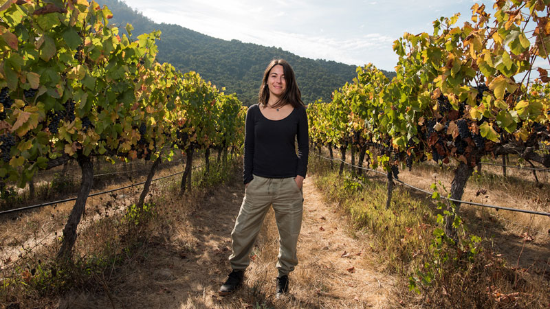 Das Bild zeigt Noelia Orts, die hauptverantworteliche Winzerin vom renommierten Weingut Emiliana in Chile, zwischen den malerischen Weinstöcken des Weinguts. Wir freuen uns sehr, verkünden zu können, dass ein Wein von Emiliana Teil der Weinverkostungen "Winzerinnen" sein wird.