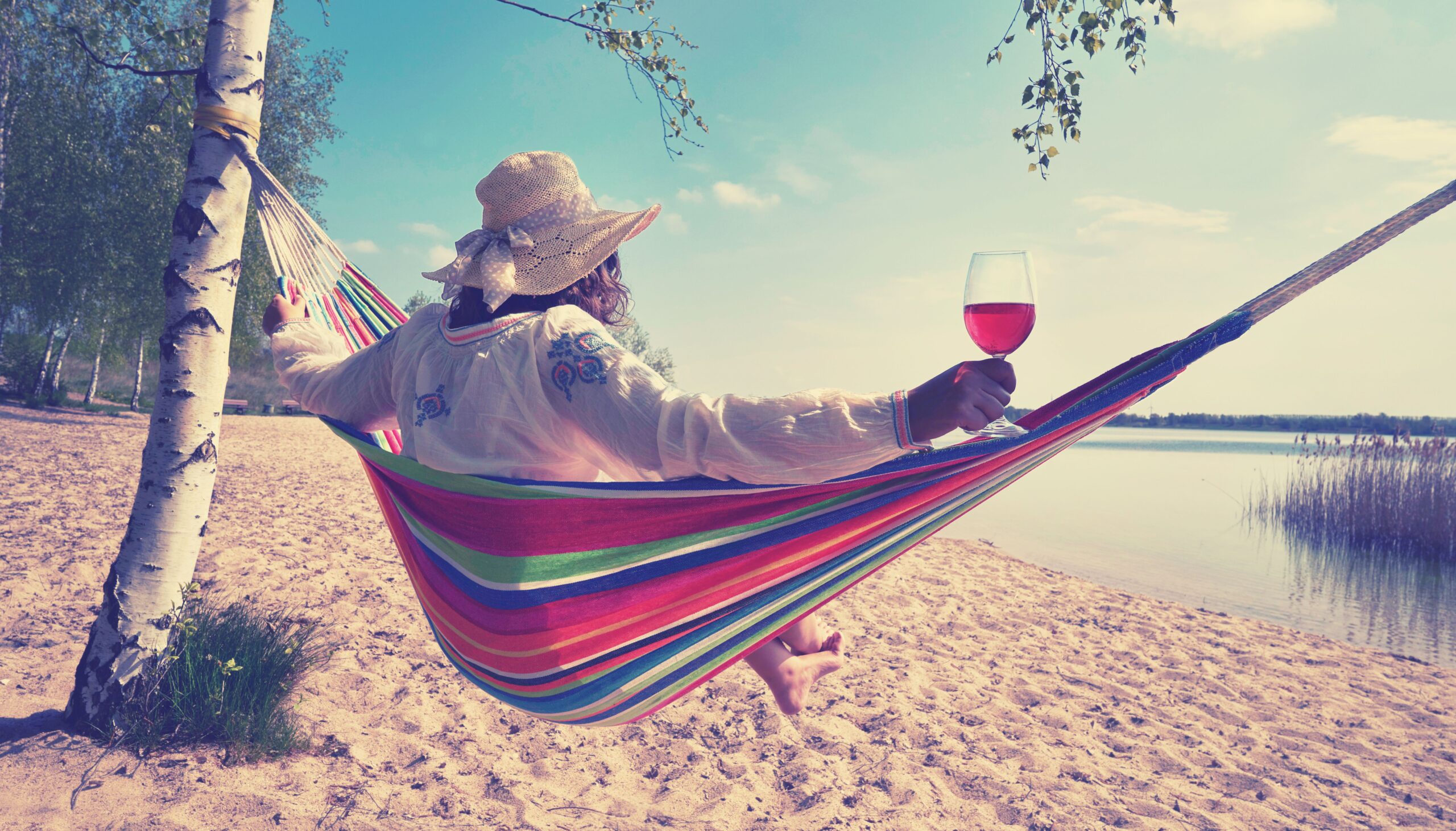 Bild zu meditarrenen Urlaubsweine - eine Frau am Strand in einer Hängematte mit einem Glas Wein in der Hand.